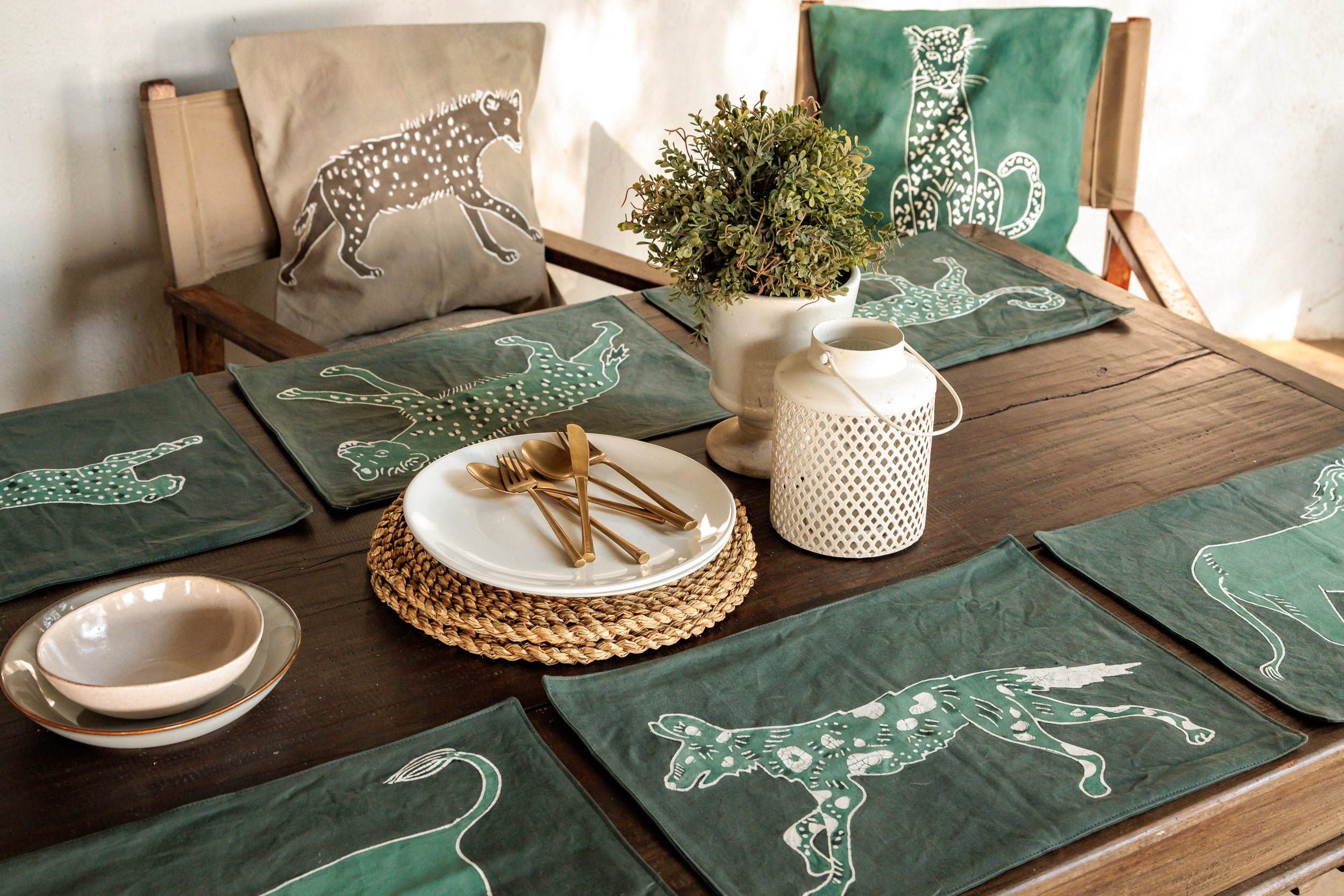 Dining table set with green placemats featuring wild safari animal designs, handcrafted batik that supports conservation efforts.