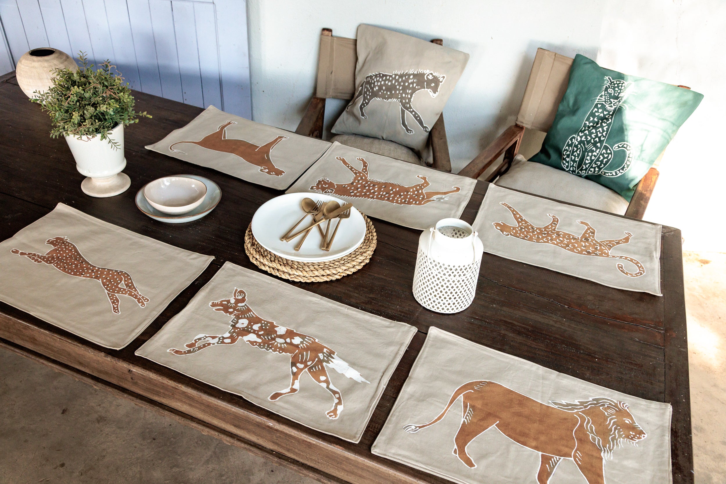Table setting with wild safari animal-themed placemats and pillows on a wooden table.