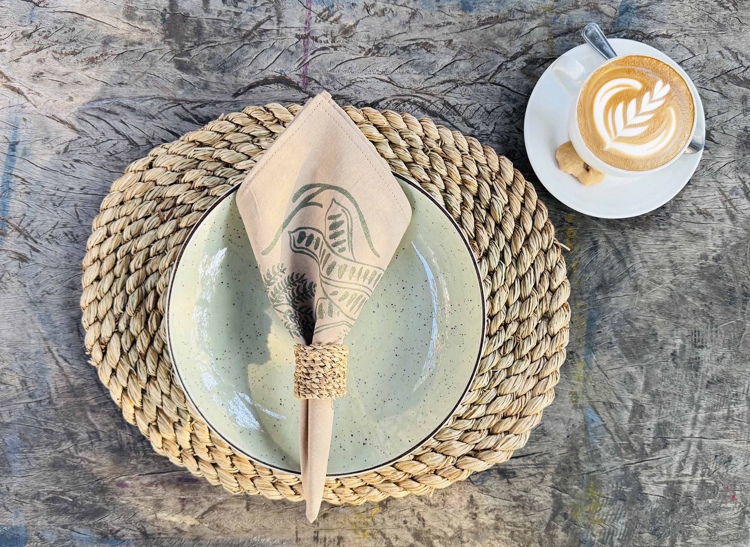 Beige cotton napkin with green hand-printed leaf design, styled on a rustic table setting, ethically handcrafted in Zambia for sustainable, eco-friendly dining decor and artisan home entertaining.