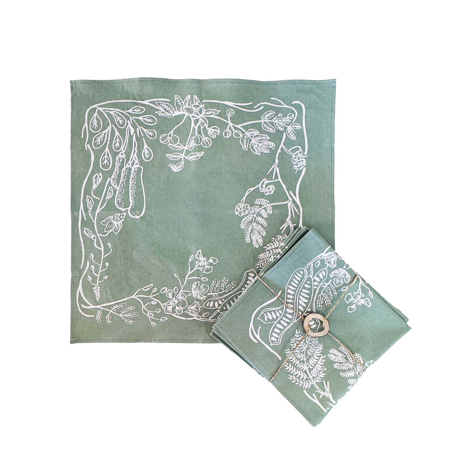 Sage green cotton napkins with subtle hand-printed leaf patterns, neatly folded on a wooden table, ethically handcrafted in Zambia for sustainable, eco-friendly dining and artisan home decor.