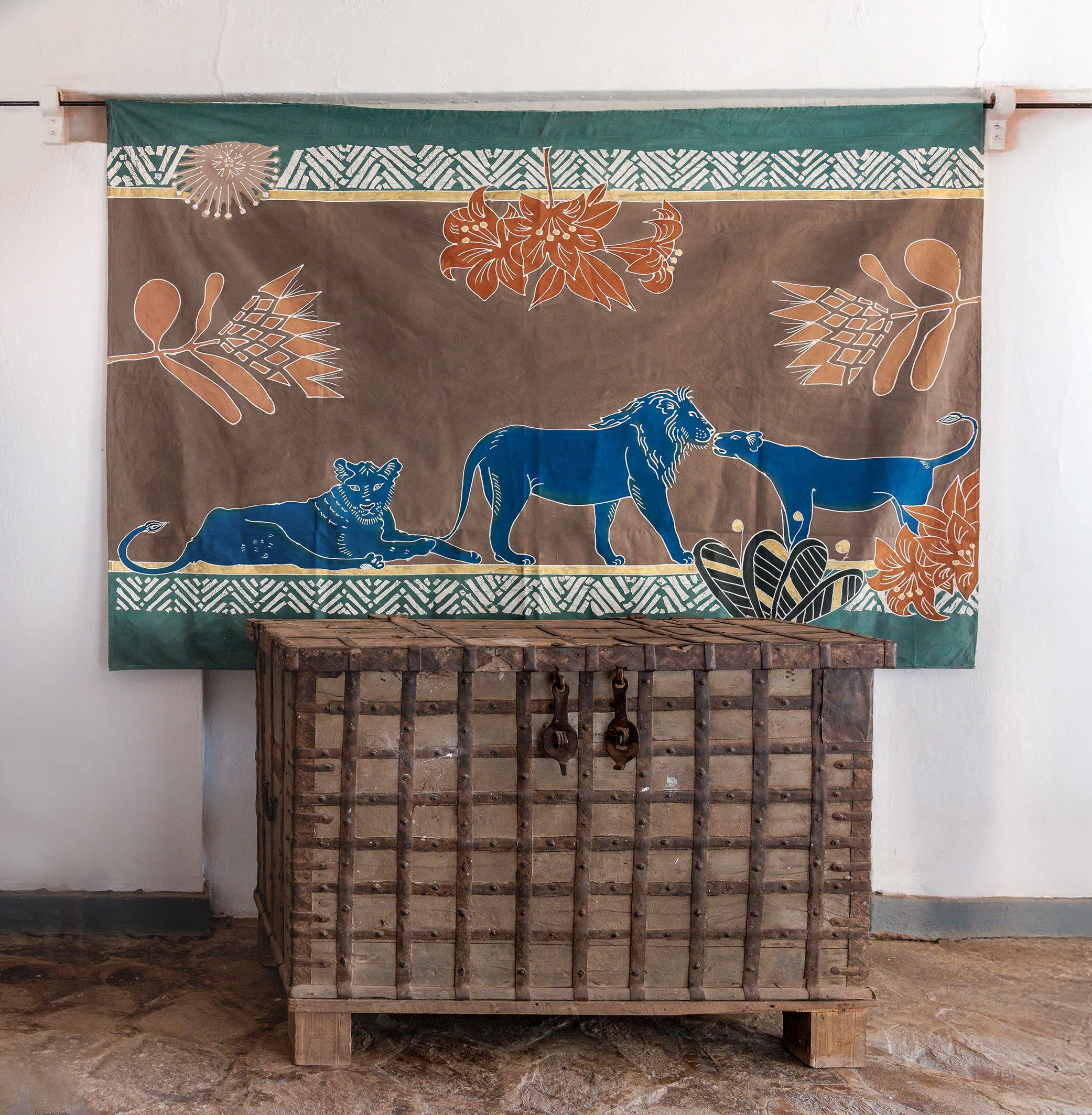 Decorative tapestry with blue lions and floral patterns hanging above a wooden chest.