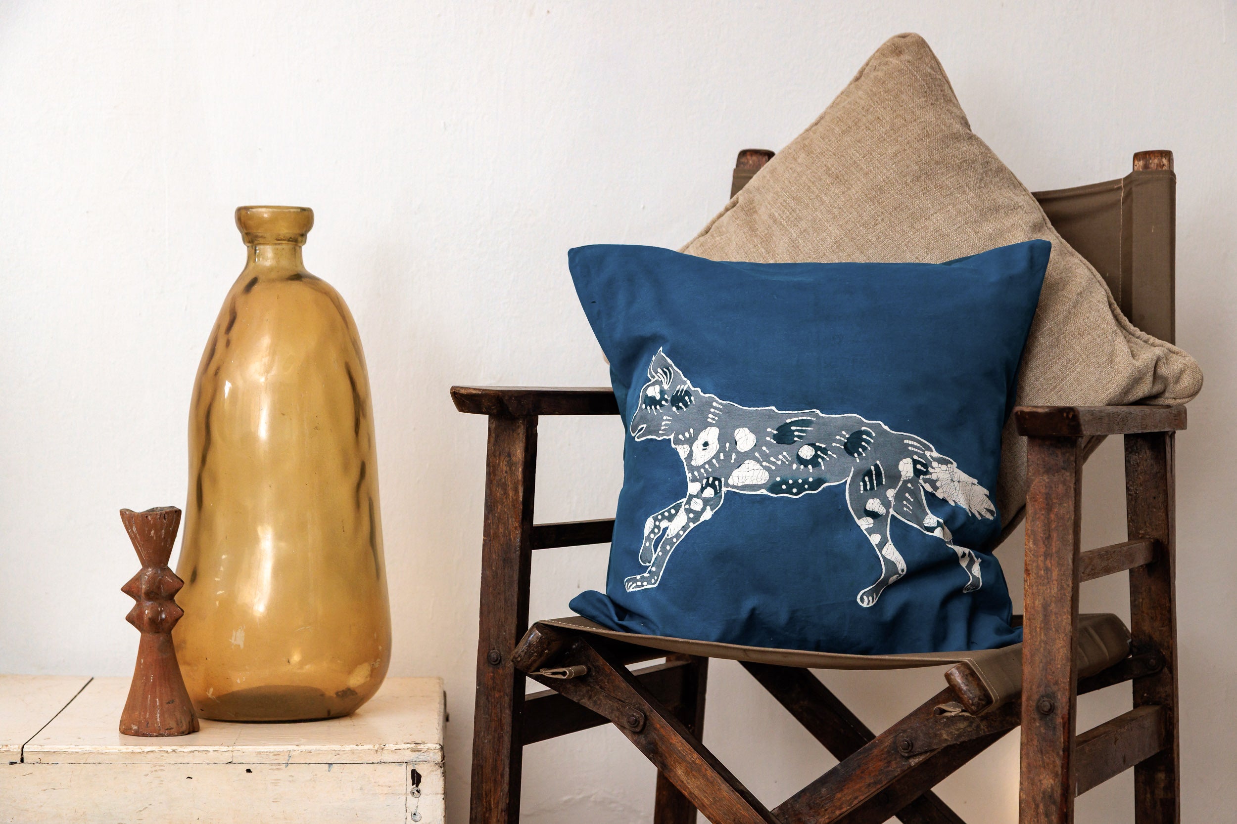 Decorative pillow with a painted dog design on a wooden chair next to a vase and small sculpture.