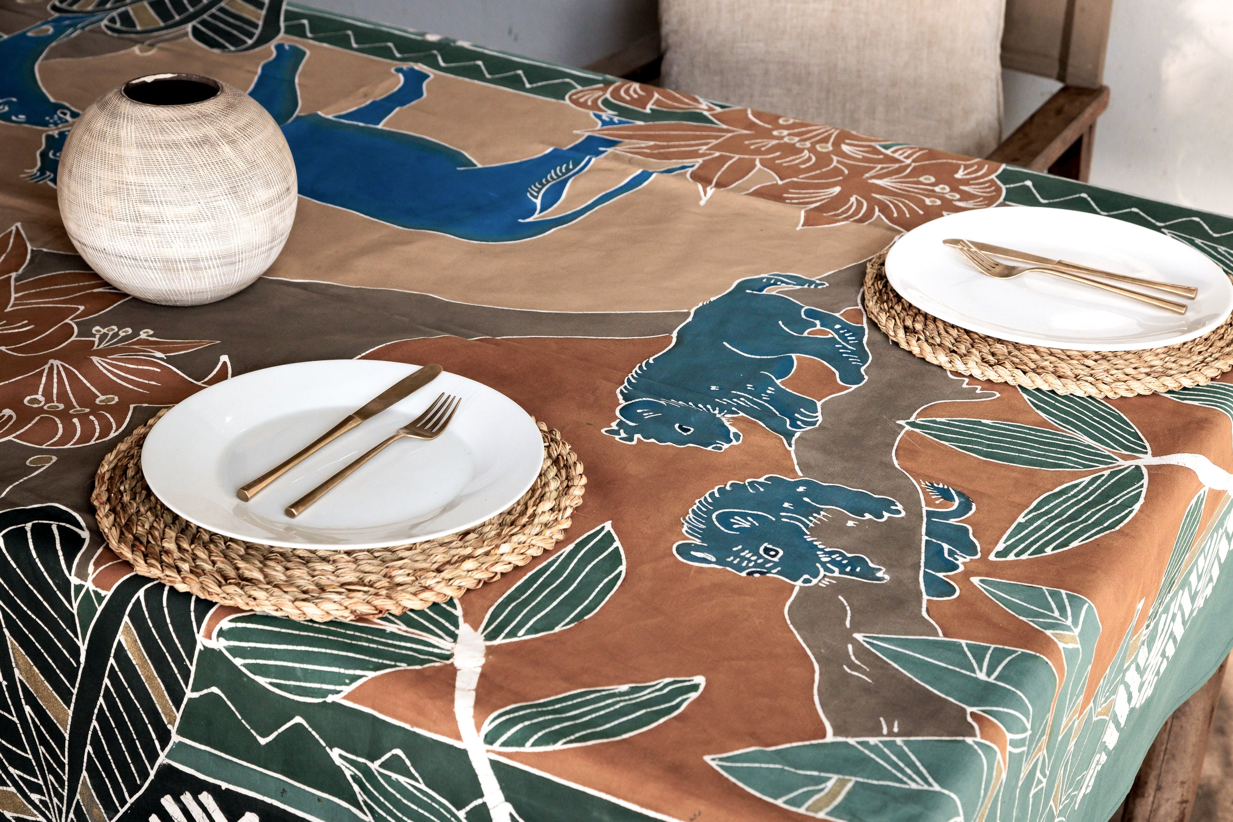 Table setting with a decorative tablecloth featuring lion cubs and lionshand painted batik from Africa.