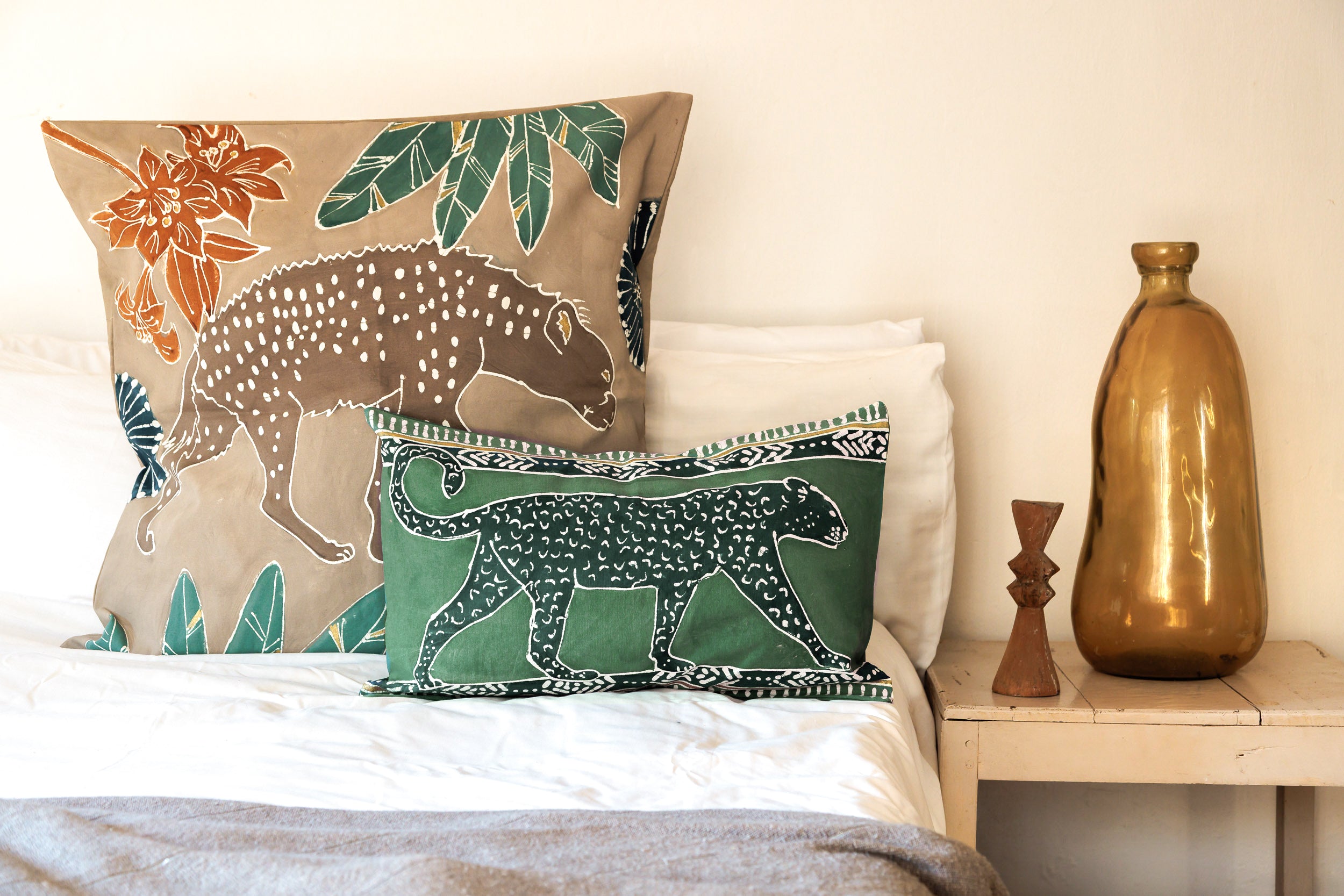 Decorative pillows with animal prints on a bed next to a nightstand with a vase.
