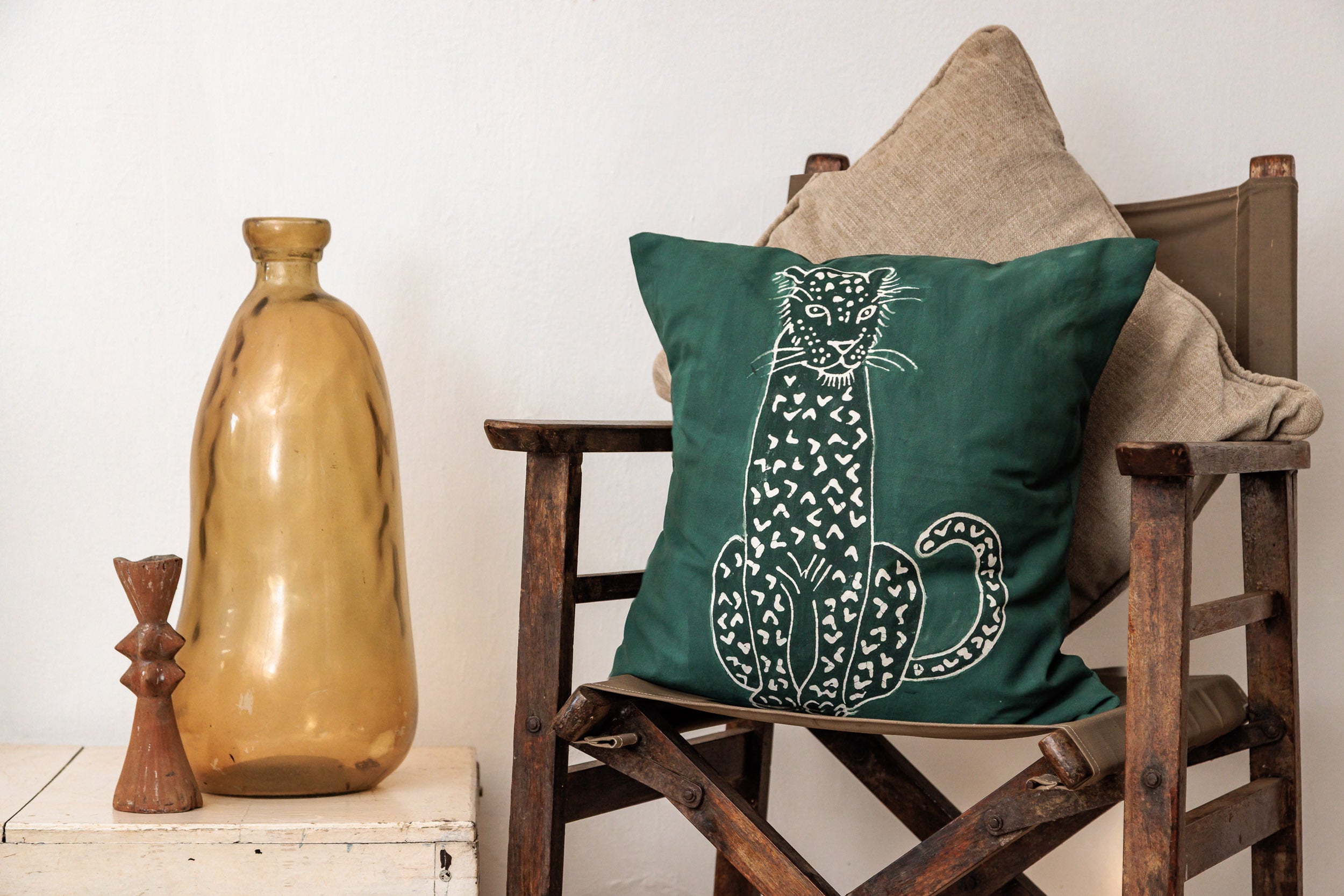 Green pillow with a leopard animal design on a wooden chair against a white wall.