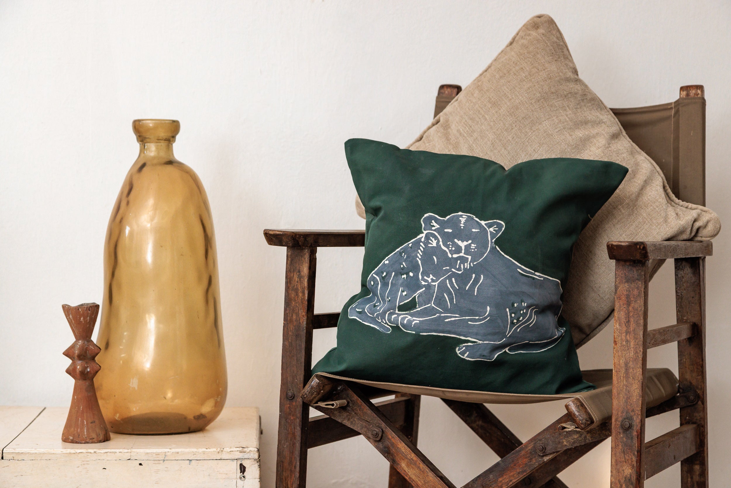 Green pillow with a lion design on a wooden chair next to a brown vase.