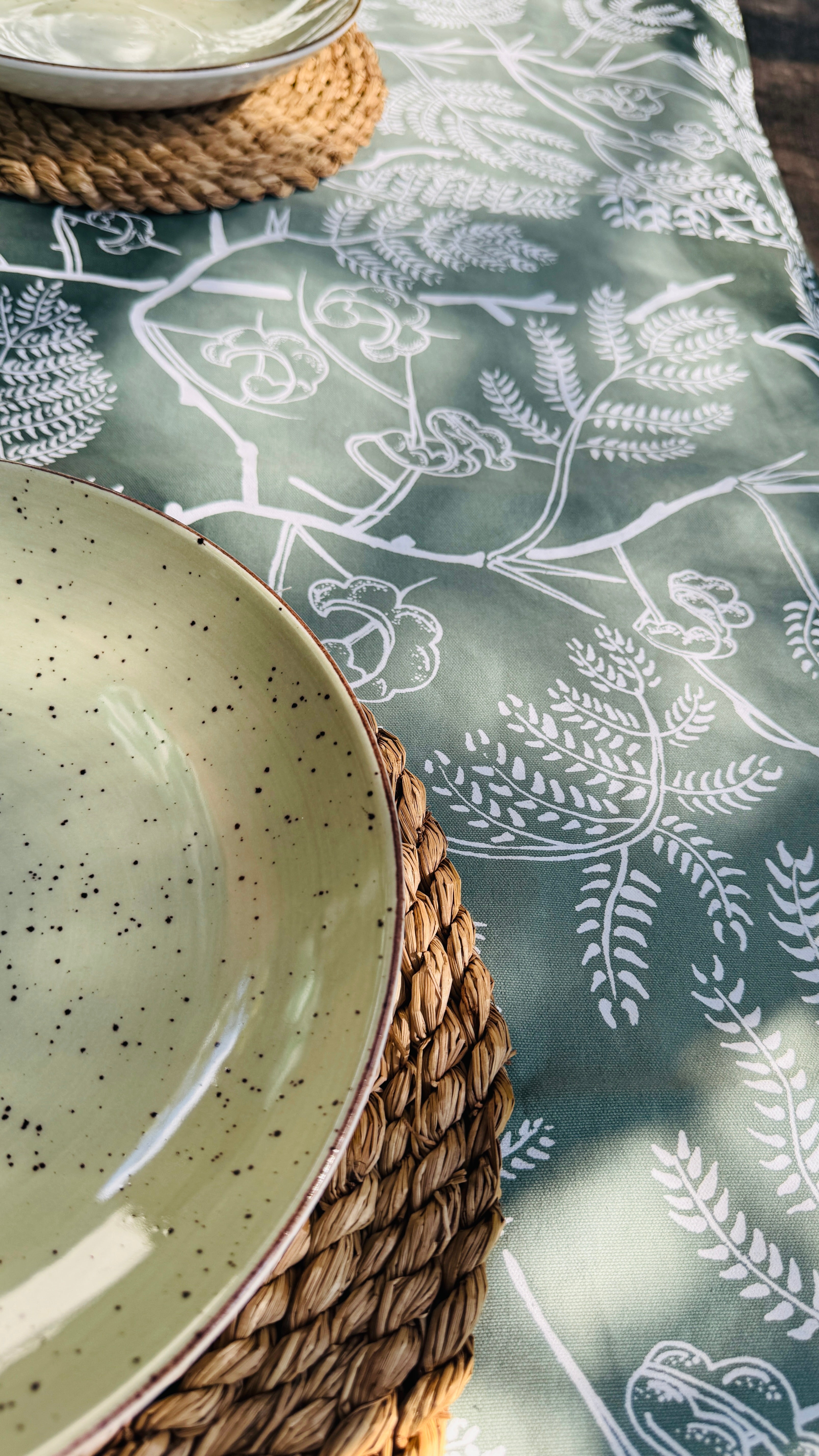 Close-up of green cotton table runner with layered leaf motifs in varying shades, ethically handcrafted in Zambia for sustainable, eco-friendly home decor, artisan craftsmanship, and fair trade interiors.
