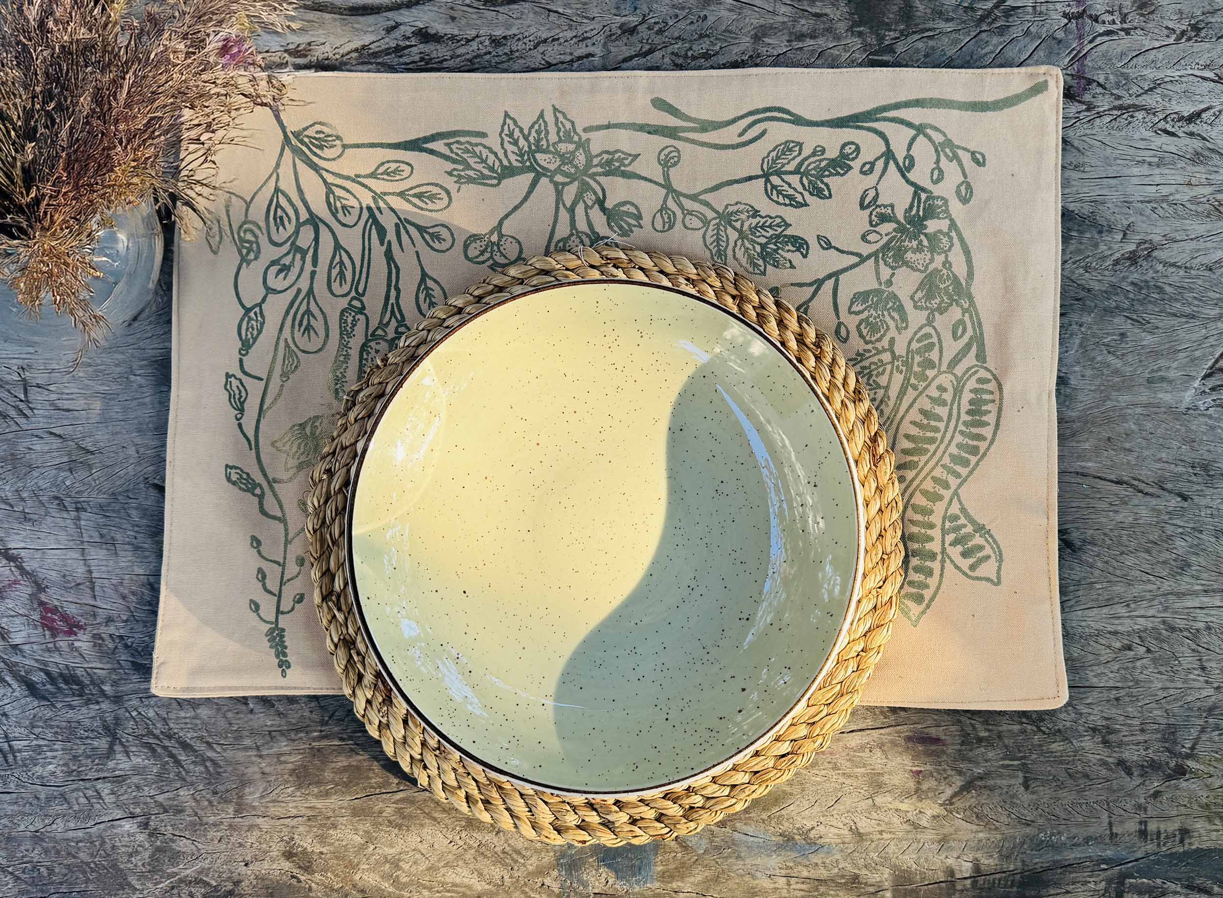 Beige cotton table mats with hand-printed green leaf designs, ethically handcrafted in Zambia for sustainable and eco-friendly dining room decor and artisan home interiors.

