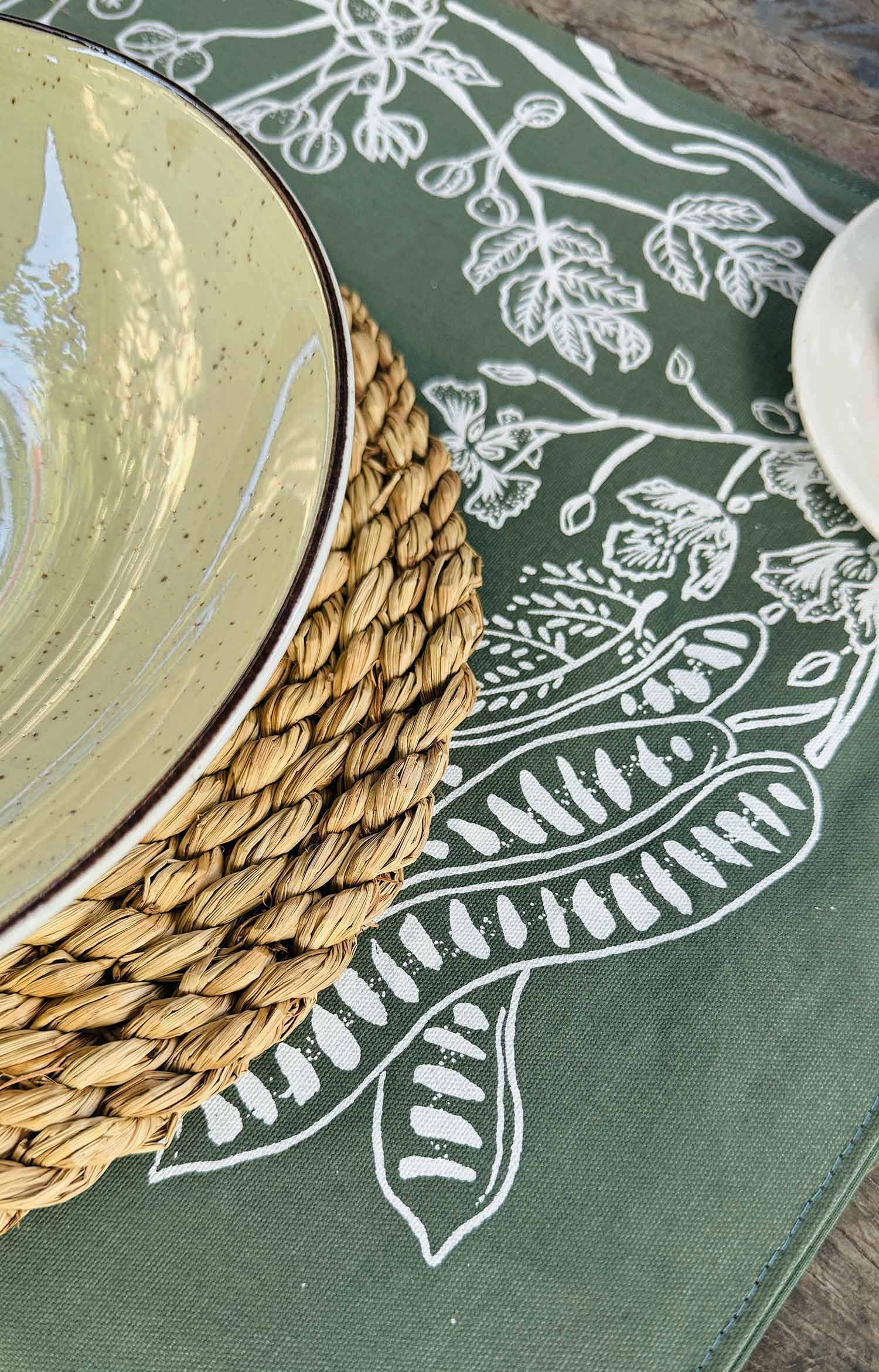 Close-up of forest green cotton table mat with layered hand-printed leaf motifs, ethically handcrafted in Zambia for sustainable, eco-friendly dining decor and artisan interiors.
